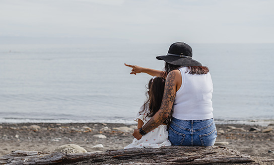Child and mother sit on beach looking out to sea